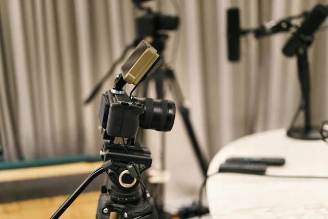 Video camera on a tripod in front of studio microphones