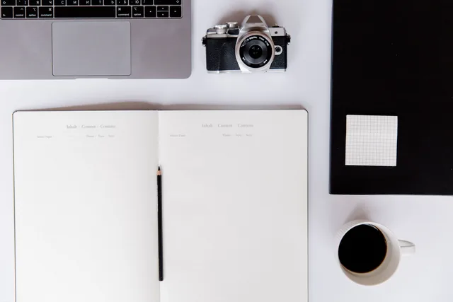 Creative desk with a camera, open notebook and coffee